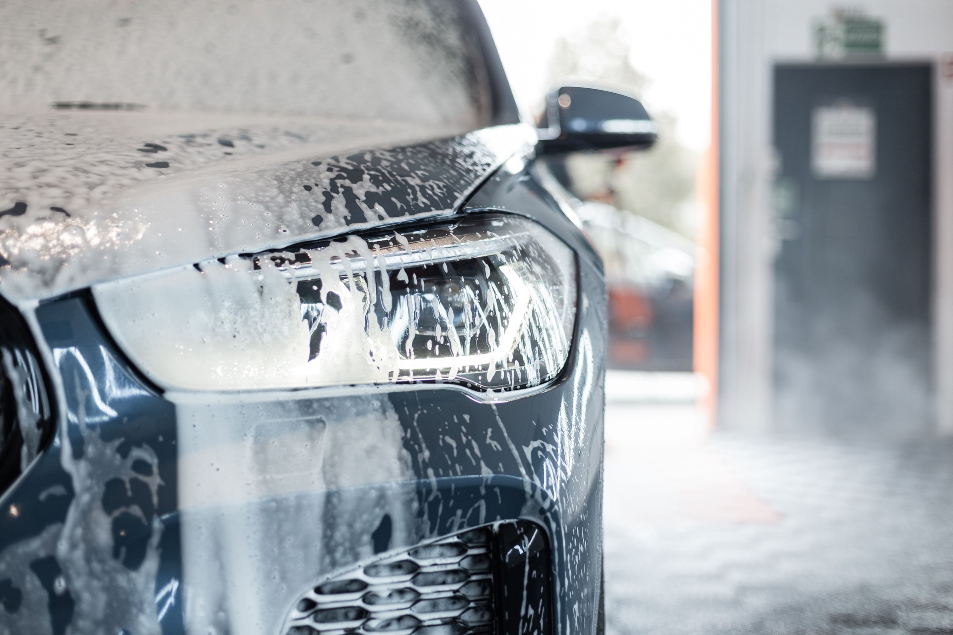Car with optics in foam at the car wash in the garage. Car care and car wash in the detailing center